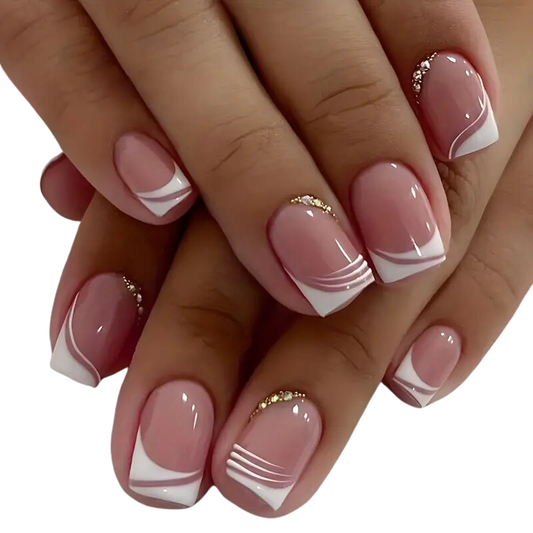 Close-up of hands flaunting Snazzi Nails Glossy Rhinestone Nails. The salon-worthy manicure features a French white edge, pink polish with subtle lines, and elegant gold accents near the cuticles.