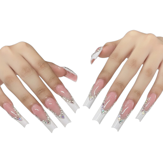 A pair of hands displaying long, coffin-shaped press-on nails with a glossy pink base, white tips, and silver rhinestone embellishments, set against a plain white background.