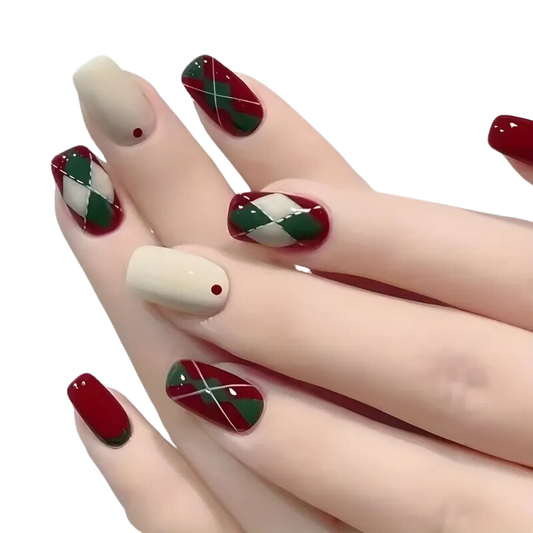 Close-up of a hand with salon-worthy, DIY Snazzi Nails. The Rhomba Nails feature red polish and an argyle pattern in red, green, and cream. One nail is cream with a small red dot at the cuticle, highlighting their elegance.