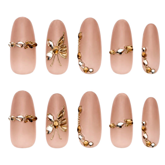 Ten nude oval press-on nails with gold-tone butterfly embellishments, amber-toned gems and champagne crystal accents.