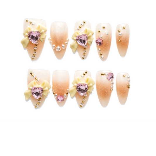 Snazzi Pink Shop Darling Dearest long almond press-on nails with nude ombre, ivory bows, pink hearts, and pearls.