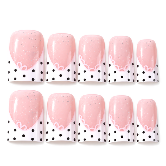 Snazzi Pink Shop short duckbill press-on nails with blush pink shimmer, white lace tips, and black polka dot accents.